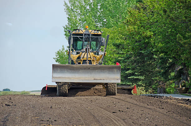 A road grader at work. It is turning and leveling the surface of a road in the process of resurfacing.